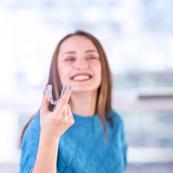 Woman smiling and holding a clear Invisalign aligner