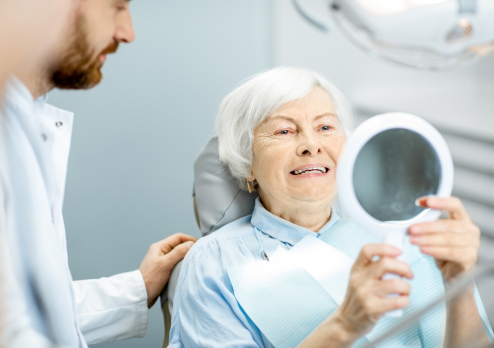 Older lady smiling into a mirror after her ceramic zirconia implant consultation in Shepperton